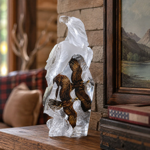 Lucite sculpture of two eagles in flight on a wooden surface with a rustic background. Title of sculpture is Valor. Artist: Kitty Cantrell