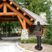 Bigfoot statue holding a 'Beware of Bigfoot' sign in front of a log and stone building.
