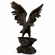 Bronze-finished sculpture of a eagle with wings spread wide, standing on a rocky base against a plain white background.