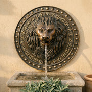 Bronze lion head fountain on a beige wall with decorative elements.