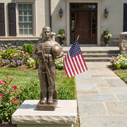 Bronze statue of a soldier holding an American flag in front of a house.