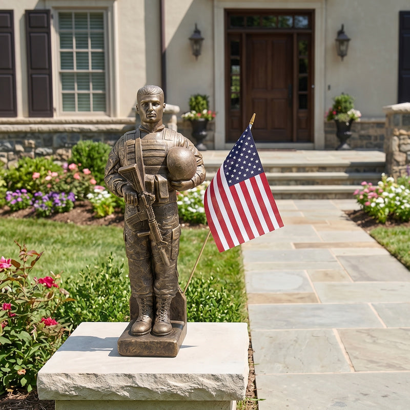 Bronze statue of a soldier holding an American flag in front of a house.