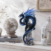 Small decorative dragon statue on a shelf with books and decorative items.