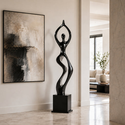 A glossy black and silver abstract sculpture of a stylized female figure standing on a rectangular pedestal, displayed in a modern interior hallway next to a large abstract wall painting.