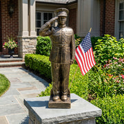Bronze garden statue of a US Marine saluting with an American flag in front of a house.