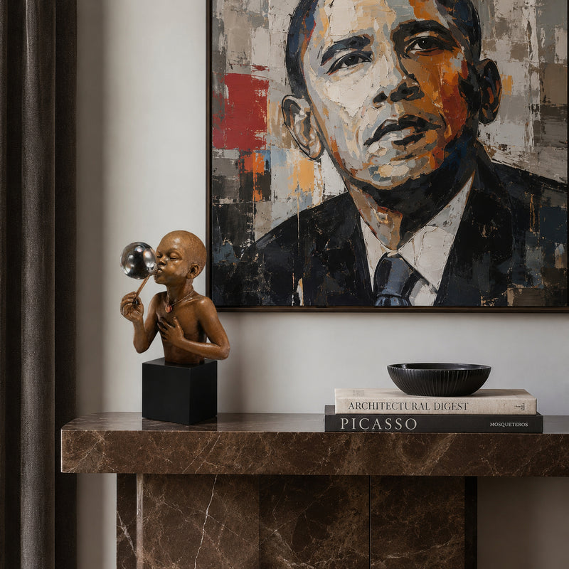 Marble console table with sculpture of a African American boy blowing bubbles, books, and framed portrait of Barack Obama on a wall.