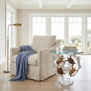 Beige armchair with a blue blanket in a bright room with large windows. End table with a turtle design.