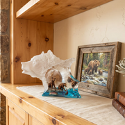 Decorative bear sculpture on a wooden shelf with a framed picture of bears in a forest.