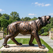 Bronze tiger statue on a pedestal with a garden and trees in the background