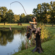 Bronze statue of a boy fishing by a pond with trees in the background