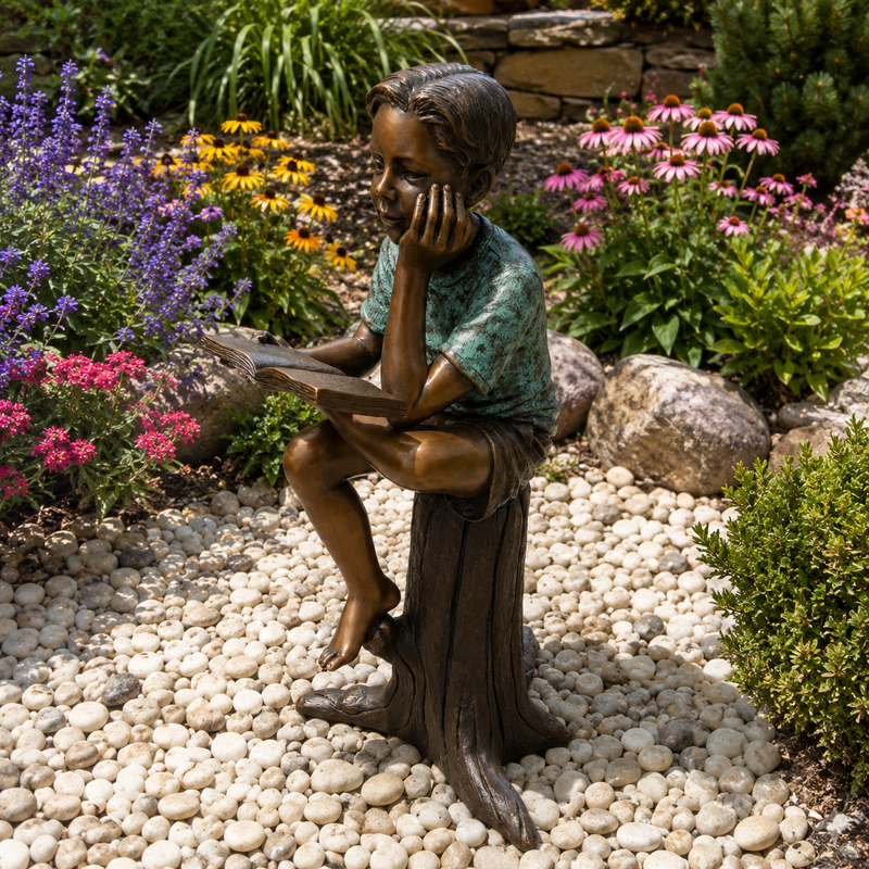 bronze statue of boy sitting on tree stump reading a book. garden type setting