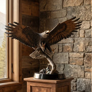 Bronze eagle statue on a wooden pedestal against a stone wall.