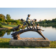 Bronze sculpture of children on a log by a pond with trees in the background