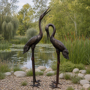 pair of bronze crane statues on edge of pond
