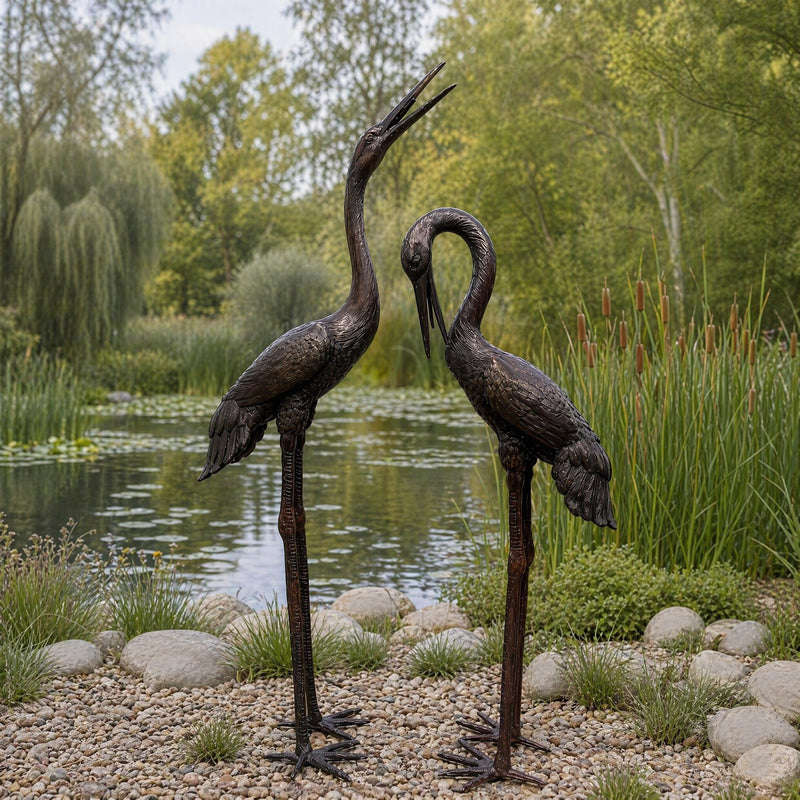 pair of bronze crane statues on edge of pond