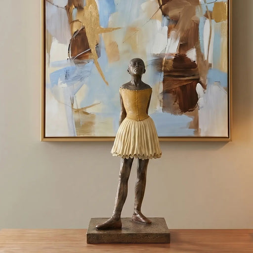Bronze sculpture of a Degas little dancer statue in front of abstract art on a wall