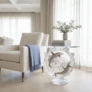 Modern living room with a glass table featuring dolphin designs, a beige armchair, and a plant.