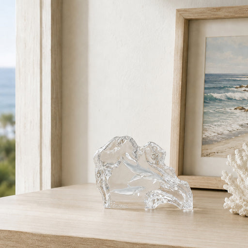 Clear sculpture on a shelf of dolphins with a framed picture of a beach in the background