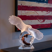 Decorative sculpture of an eagle with outstretched wings on a clear base, with a colorful abstract painting in the background.