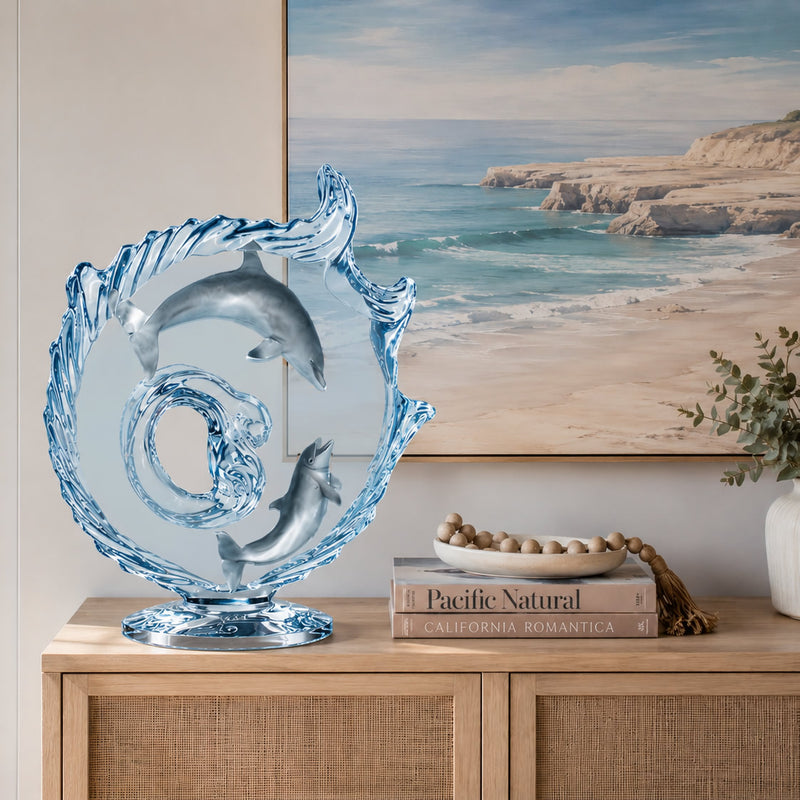 Acrylic dolphin sculpture by artist Dan Medina sitting on console table with beach painting behind.