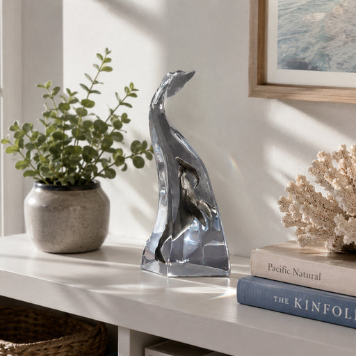 Decorative table top acrylic sculpture of a whale on a shelf with books and a plant.