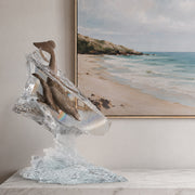 Lucite sculpture of dolphins on a table with a beach scene painting in the background
