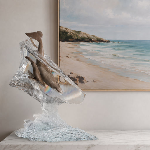 Lucite sculpture of dolphins on a table with a beach scene painting in the background