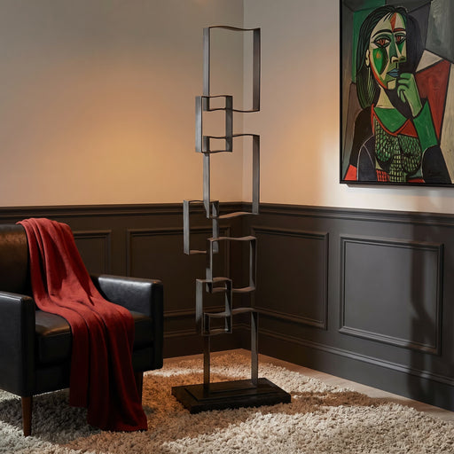 Modern iron floor sculpture with black leather chair next to it. A Picasso style painting hangs on wall.