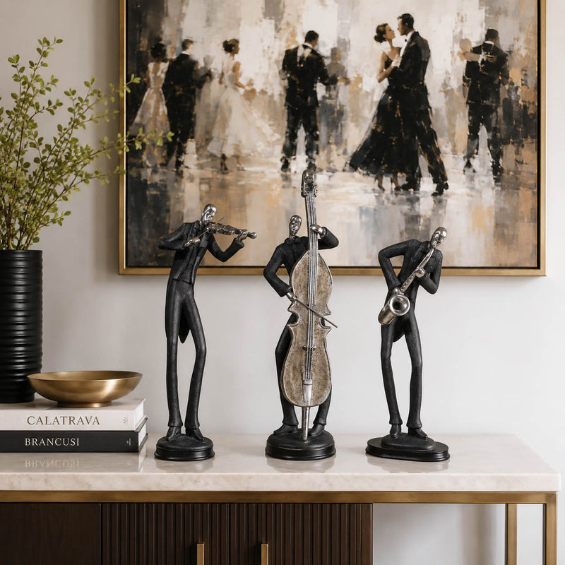 Three black metal figurines of jazz musicians (violinist, double bass player, saxophonist) displayed on a marble console table in a styled interior setting with a large dancing couple painting on the wall.