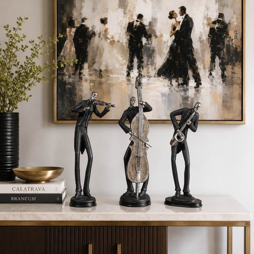 Three black metal figurines of jazz musicians (violinist, double bass player, saxophonist) displayed on a marble console table in a styled interior setting with a large dancing couple painting on the wall.