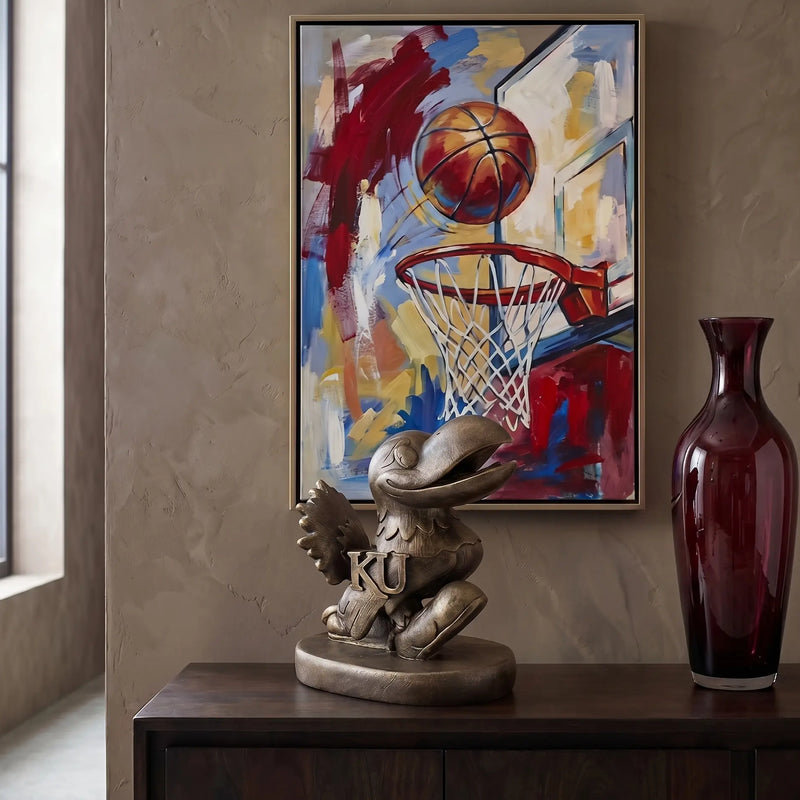 Decorative setup with a sculpture of the Kansas Jayhawks mascot statue, vase, and abstract painting of a basketball scene.
