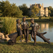 Bronze sculpture of three children on a log by a pond with a house in the background
