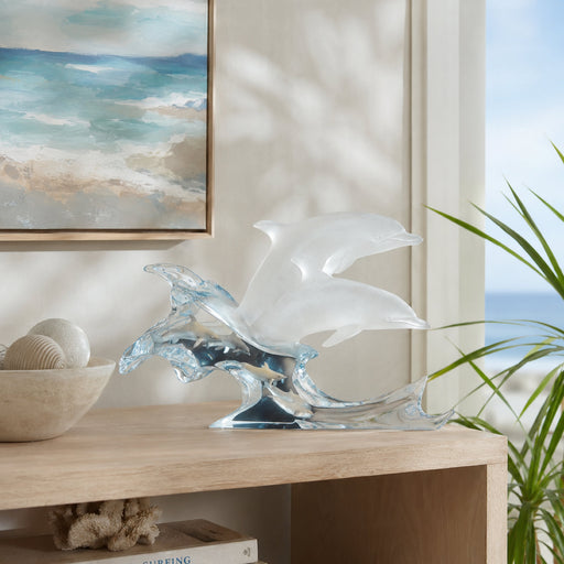 Lucite sculpture of two dolphins jumping out of a wave. sitting on table with modern accessories.