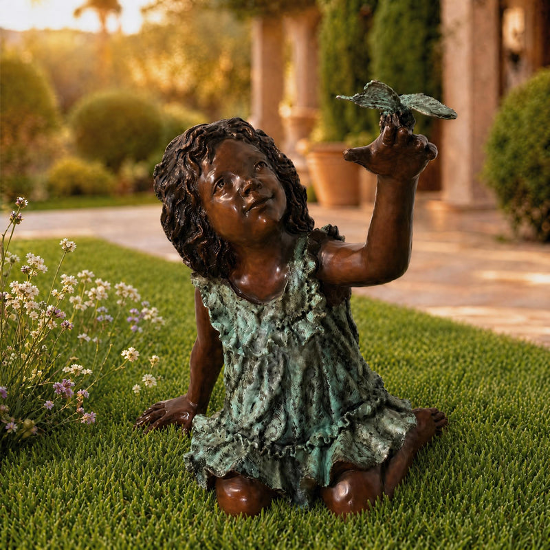 Bronze statue of a young girl holding a butterfly in a garden setting