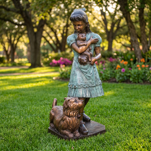 Bronze statue of a girl holding a cat and a dog on a grassy lawn with flowers and trees in the background