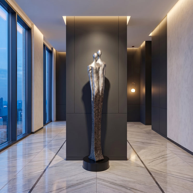 Large standing modern sculpture of a couple in silver color in a stylish interior setting with large windows