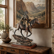 Statue of a mountain man on horseback on a wooden table with a mountain landscape painting in the background.