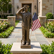 Statue of a navy sailor saluting with an American flag, set against a garden backdrop.