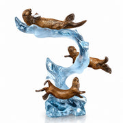 Bronze sculpture of three otters on a wave with a white background