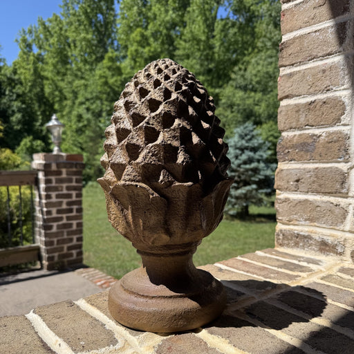 pine cone finial on brick ledge outdoors with patio and yard in background