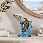Decorative sculpture of seals by artist Kitty Cantrell. Seal It with a Kiss is the title. Sitting on a shelf with books and a mirror in the background