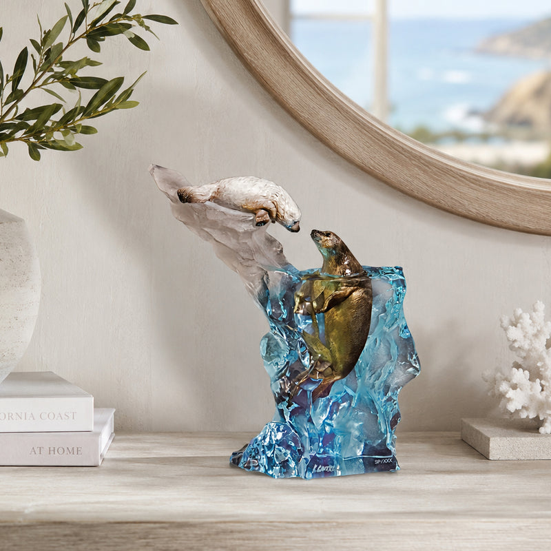 Decorative sculpture of seals by artist Kitty Cantrell. Seal It with a Kiss is the title. Sitting on a shelf with books and a mirror in the background