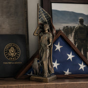 Statue of Lady Liberty holding an American flag with a framed picture of soldiers in the background.