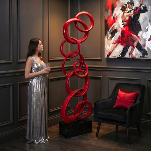 Red floor sculpture on black base. Female in silver dress admiring sculpture and modern couple painting on wall.