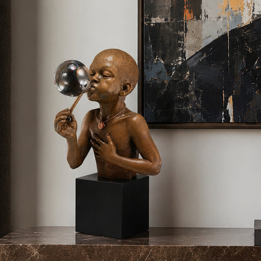Bronze sculpture of a African American child blowing a bubble on a black cube pedestal against a neutral wall with abstract art. Title of sculpture is Summer Days. Artist: Thomas Blackshear