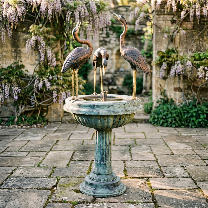 Decorative outdoor fountain with three heron statues in a garden setting.