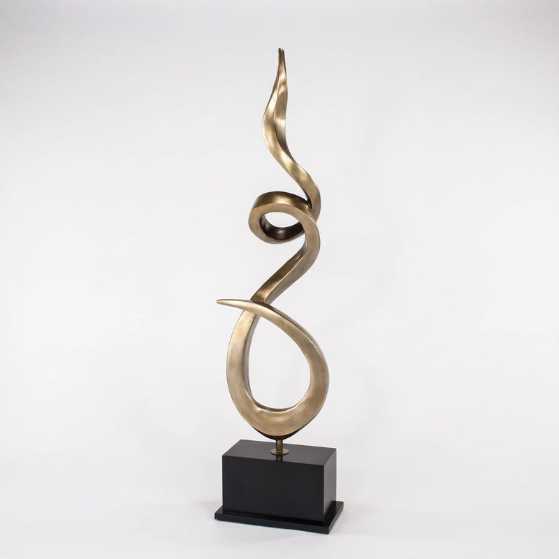 Abstract umber gold sculpture on a black base against a white background