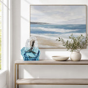 Decorative console table with a mixed media whale sculpture, white bowl, and green plant, featuring a framed beach scene painting.