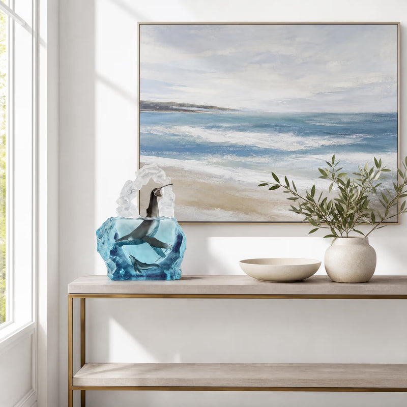 Decorative console table with a mixed media whale sculpture, white bowl, and green plant, featuring a framed beach scene painting.