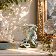 Decorative scene with a dragon statue, crystal ball, and books on a surface.